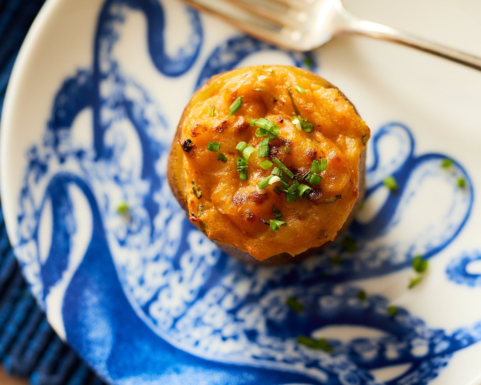 A top down view on one twice baked potato sprinkled with chives on a Lucy the octopus canapé plate.