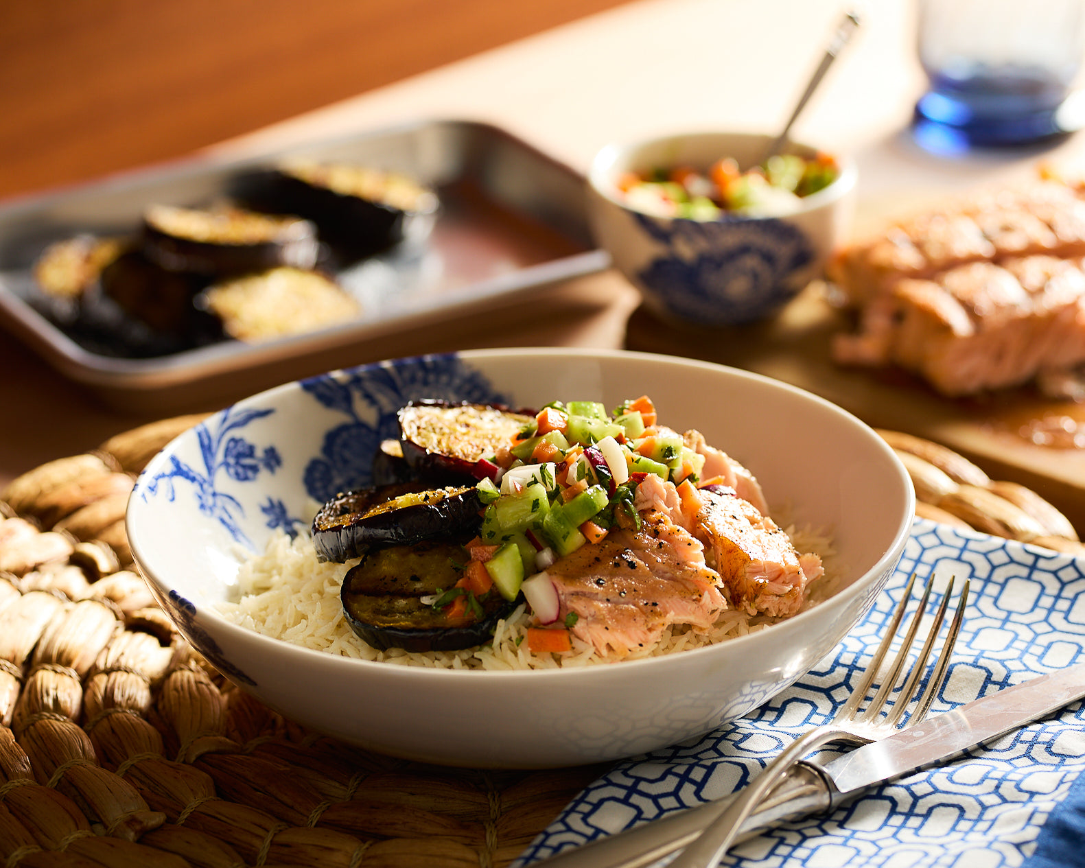 A shallow, blue and white bowl filled with rice and slices of grilled eggplant and salmon topped with salsa.