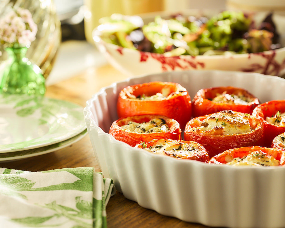 A white casserole dish full of roasted tomatoes stuffed with goat cheese.