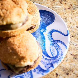 Two sesame seed burgers rest elegantly on Caskata's Lucy Melamine Dinner Plates, adorned with an octopus design, perfect for outdoor dining.