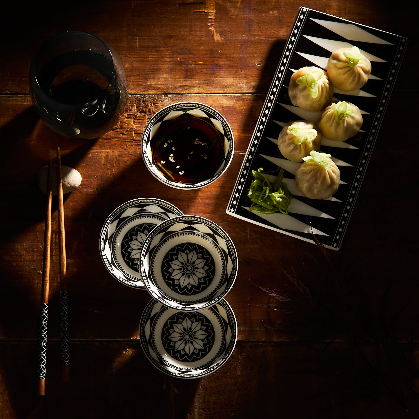 A table showcasing Caskata's Fez Dipping Dishes set with intricate patterns, alongside patterned plates, a glass, chopsticks, and a rectangular plate with dumplings and greens embodies Morocco's vibrant essence.