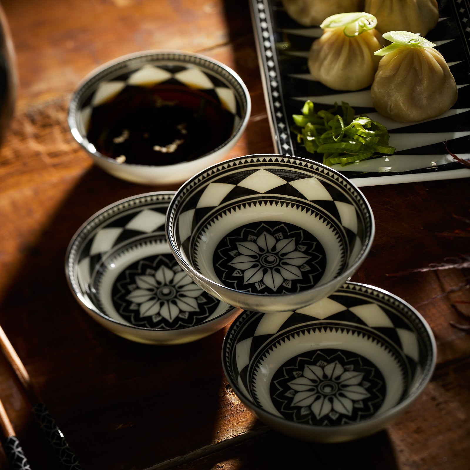 A table showcasing Caskata's Fez Dipping Dishes set with intricate patterns, alongside patterned plates, a glass, chopsticks, and a rectangular plate with dumplings and greens embodies Morocco's vibrant essence.