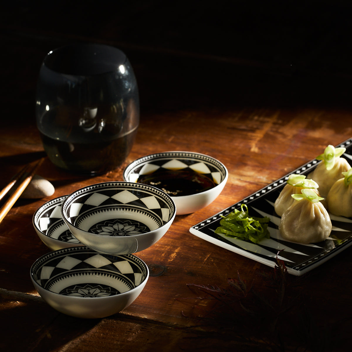 Dim sum on a rectangular plate with garnish, alongside the Caskata Fez Dipping Dishes featuring geometric patterns and a glass drink, all arranged on a wooden table evoking Moroccan textures.