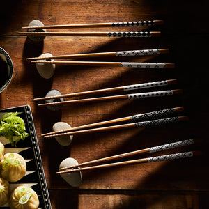 Miya, Inc.'s Nara Chopsticks with decorative handles are neatly placed on stone rests next to a dish of dumplings and a bowl of chopped green onions, creating a unique set that beautifully complements sushi trays.