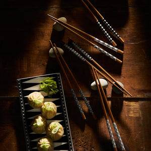 A rectangular plate with dumplings and green garnish beside a unique set of Nara Chopsticks by Miya, Inc. on a wooden table.