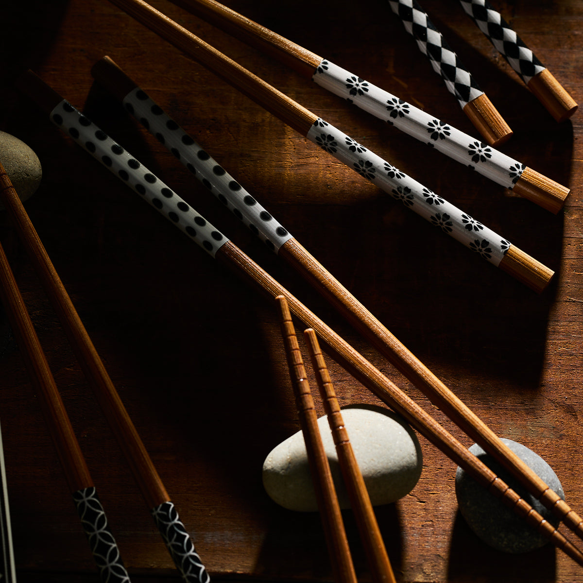 Nara Chopsticks by Miya, Inc., featuring assorted bamboo designs, are elegantly displayed among smooth round stones, perfectly poised to complement your sushi trays.