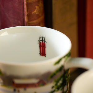 Close-up of a white porcelain mug from the Caskata X Felix Doolittle Winter Wonderland set, adorned with an intricate red sled illustration that evokes a picturesque New England atmosphere.