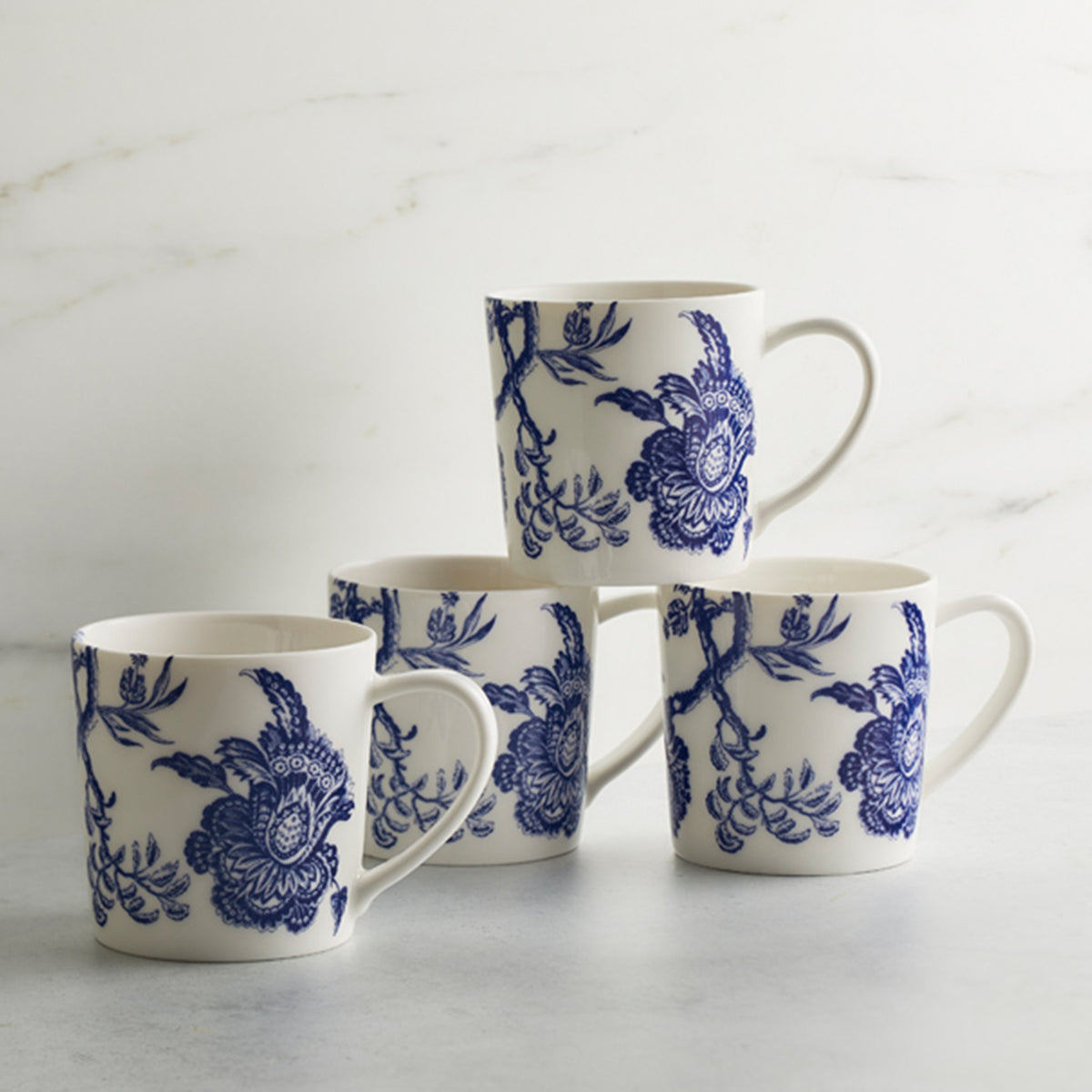 Four Arcadia Mugs by Caskata Artisanal Home, inspired by the Williamsburg Foundation, are arranged on a light gray surface against a white marble background.