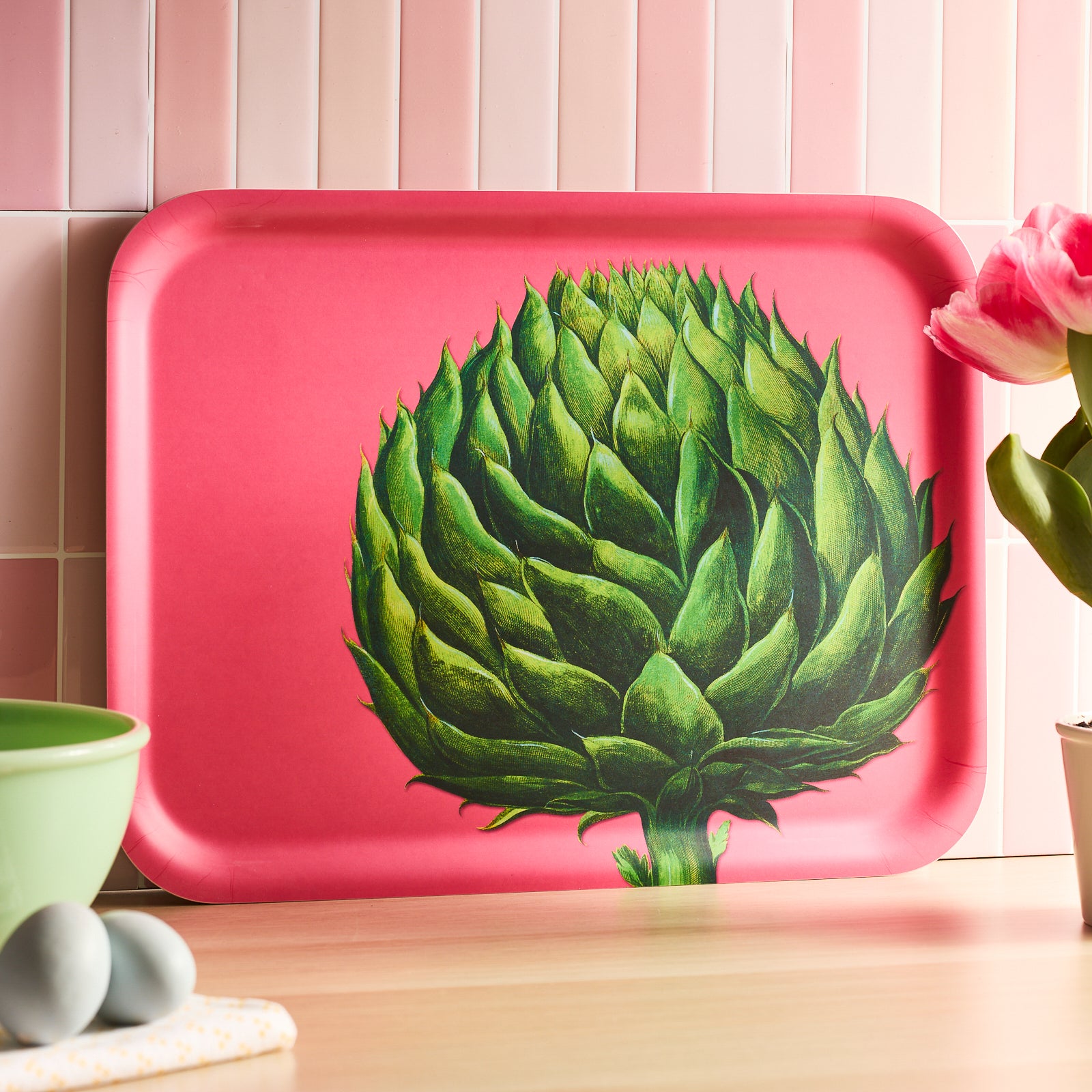 The Artichoke Large Rectangular Birchwood Tray by Caskata features a green artichoke on a vivid pink background, perfect for adding a pop of color to your sustainable decor.