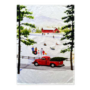 A red truck carrying a tree is parked by a snowy field, capturing the essence of winter charm. Families are sledding and playing nearby, with a red barn and pine trees in the backdrop, much like the delightful illustration found on the Caskata X Felix Doolittle Winter Wonderland Kitchen Towels, Set of 2 by Caskata.