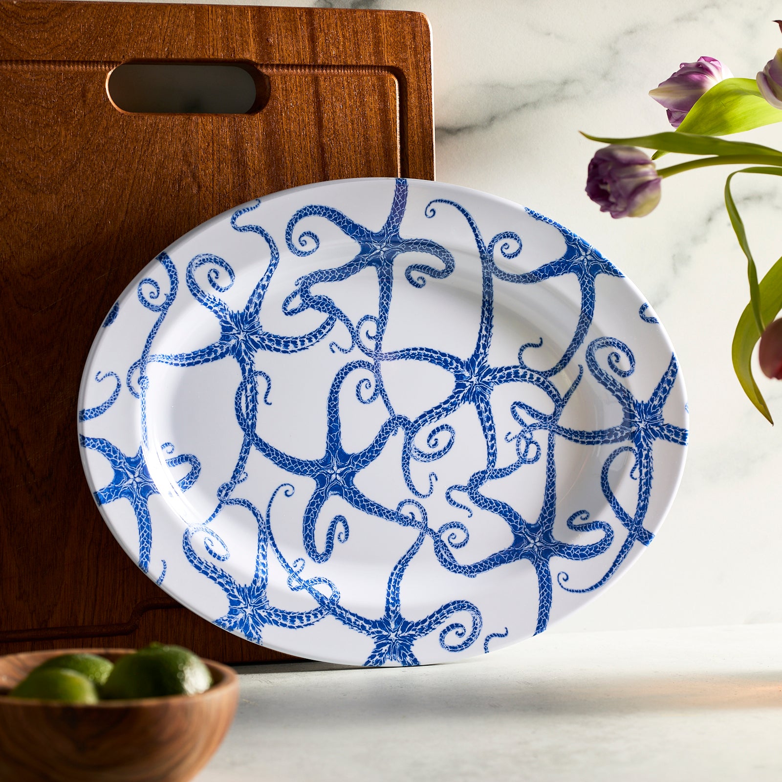 The Caskata Starfish "Dinner is Served" Melamine Bundle is a BPA-free dinnerware set showcasing vibrant blue octopus designs on each white plate and bowl, ideal for stylish outdoor dining.