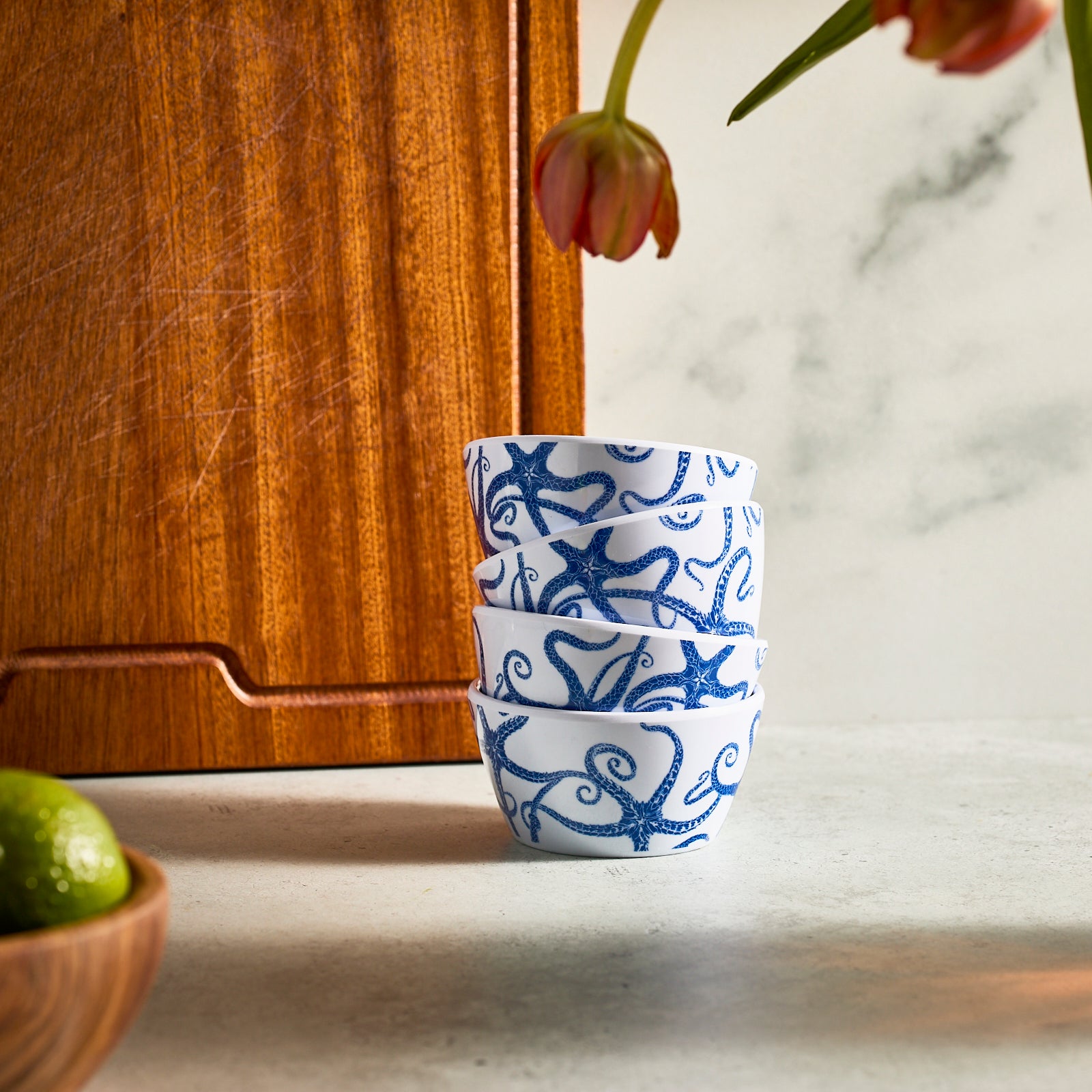 A stack of four Caskata Starfish Melamine Snack Bowls featuring a starfish design sits on a beige surface, with one separated on the right. These BPA-free bowls combine unbreakable style and practicality for any setting.