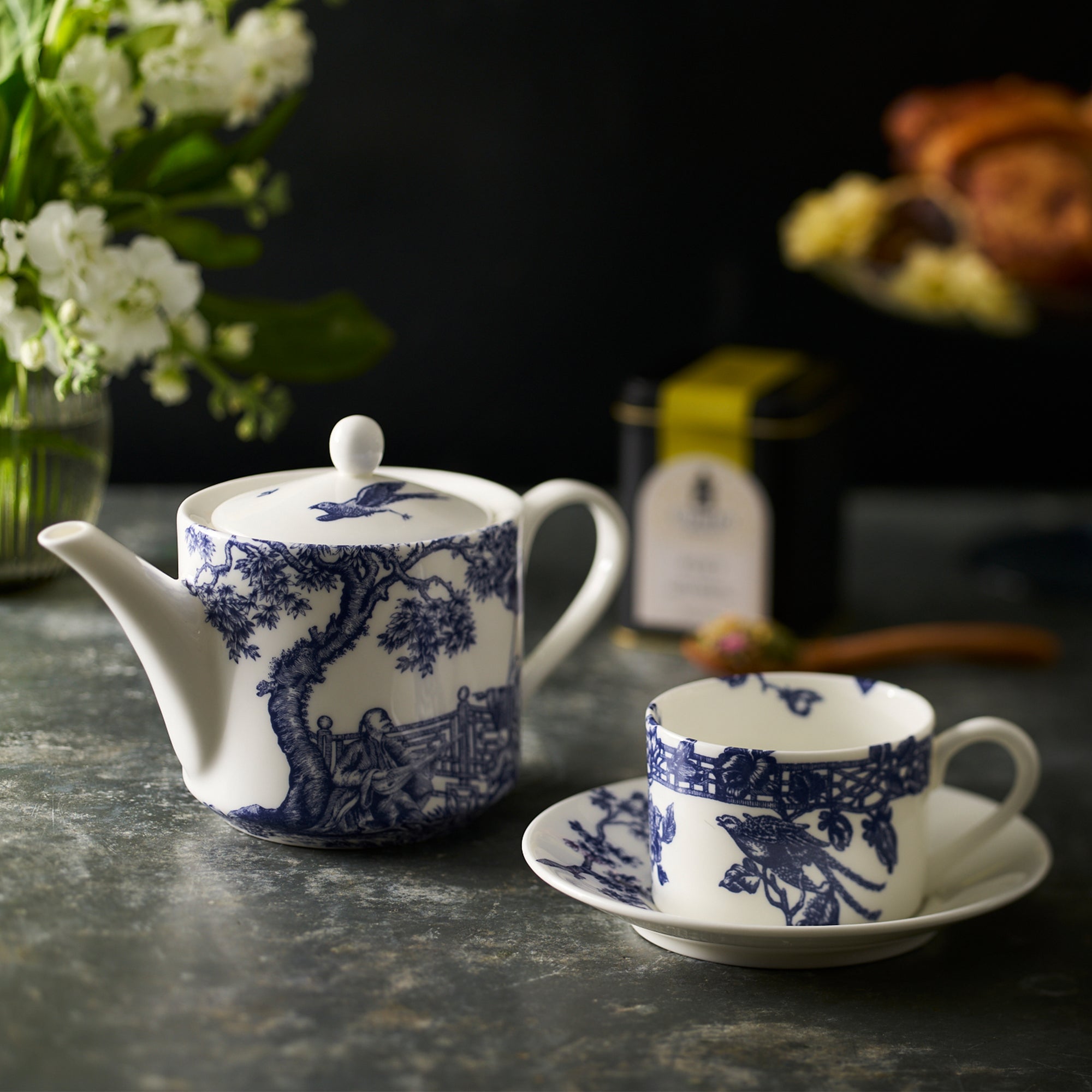 The Chinoiserie Tea Bundle by Caskata includes a white bone china teapot, creamer, two cups, and matching saucers with blue architectural and nature designs echoing Chinoiserie Toile elegance.