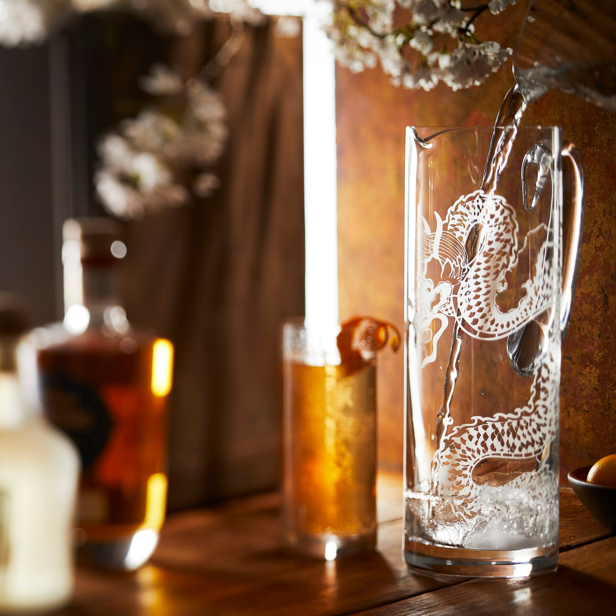 The Dragon Glassware Bundle by Caskata includes four lead-free crystal pieces: two intricately sand-etched dragon design pitchers and two tall glasses.