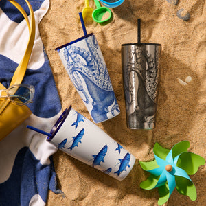 Three Caskata Lucy Chrome Stainless Steel Insulated Tumblers feature vibrant octopus and fish patterns as they sit on a sandy beach, accompanied by a yellow bag, sunglasses, beach toys, and a towel.