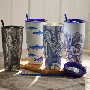 Four Lucy Chrome Stainless Steel Insulated Tumblers by Caskata, adorned with ocean-themed designs of octopuses and sharks, are arranged on a wooden tray. Accompanied by blue lids and straws, these stunning tumblers guarantee to maintain your drinks at the ideal temperature.