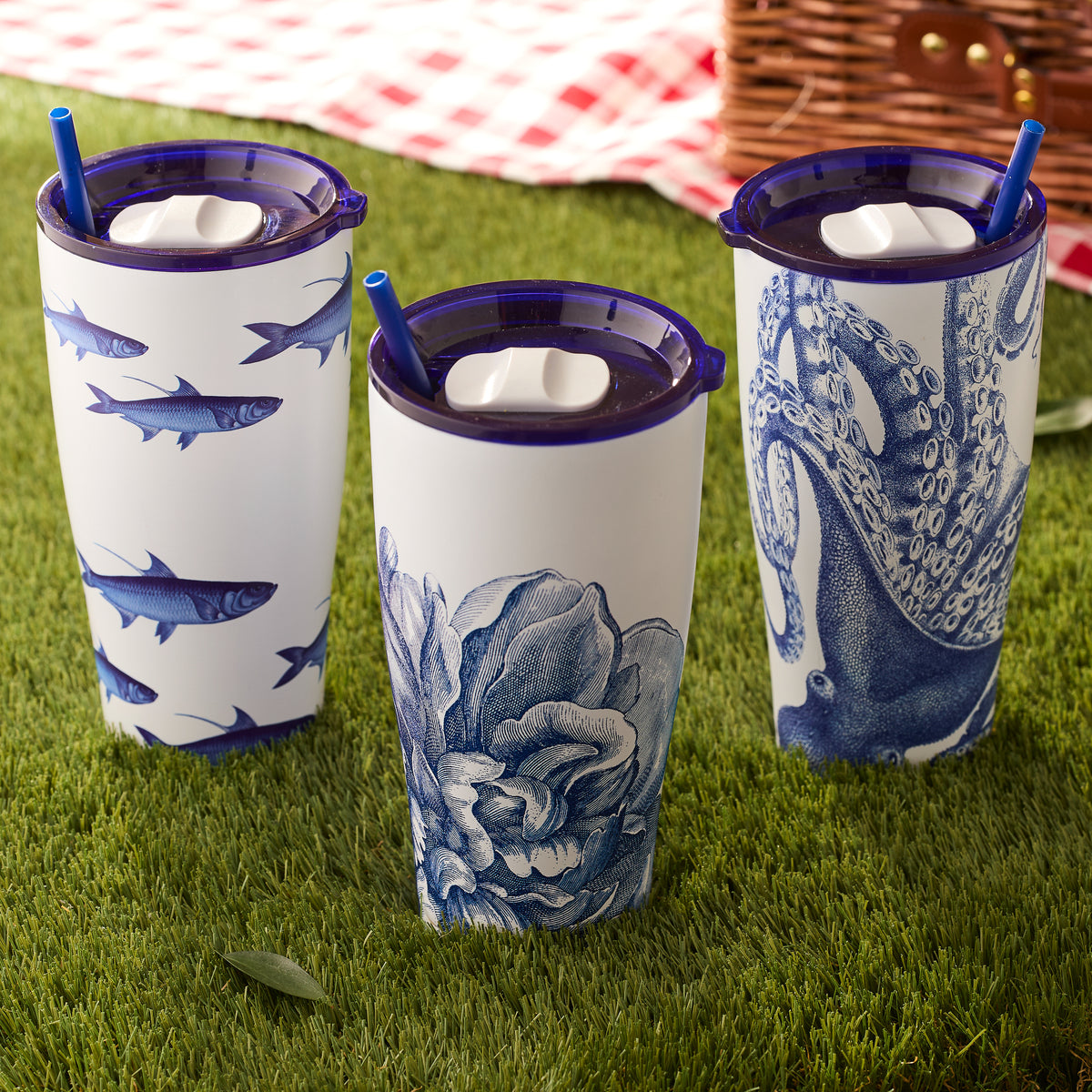 Three Lucy Stainless Steel Insulated Tumblers by Caskata, featuring blue designs of fish, flowers, and an octopus, elegantly grace the grass.