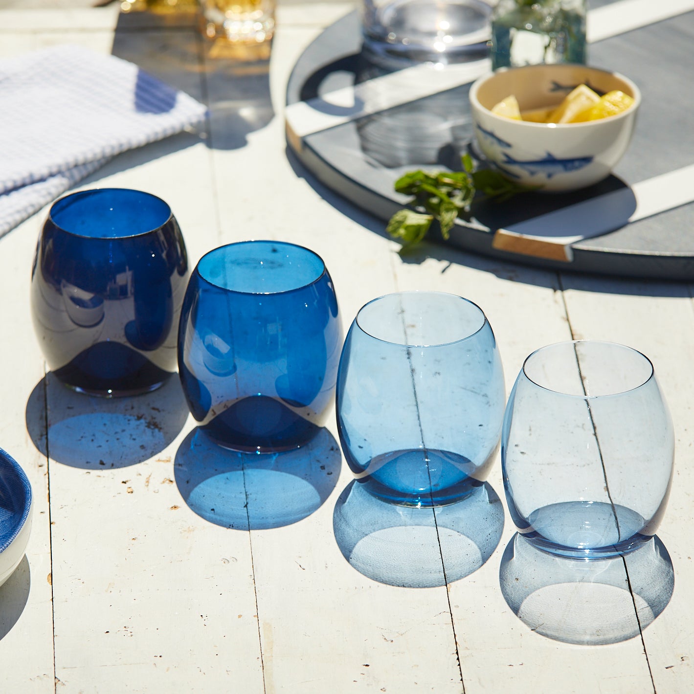A Host With the Most Bundle from Caskata, which includes a set of four Blue Lobster Small Plates, four Les Nuages Tumblers with a blue gradient, a clear glass Les Nuages Pitcher with a blue handle, and blue lobster napkins.