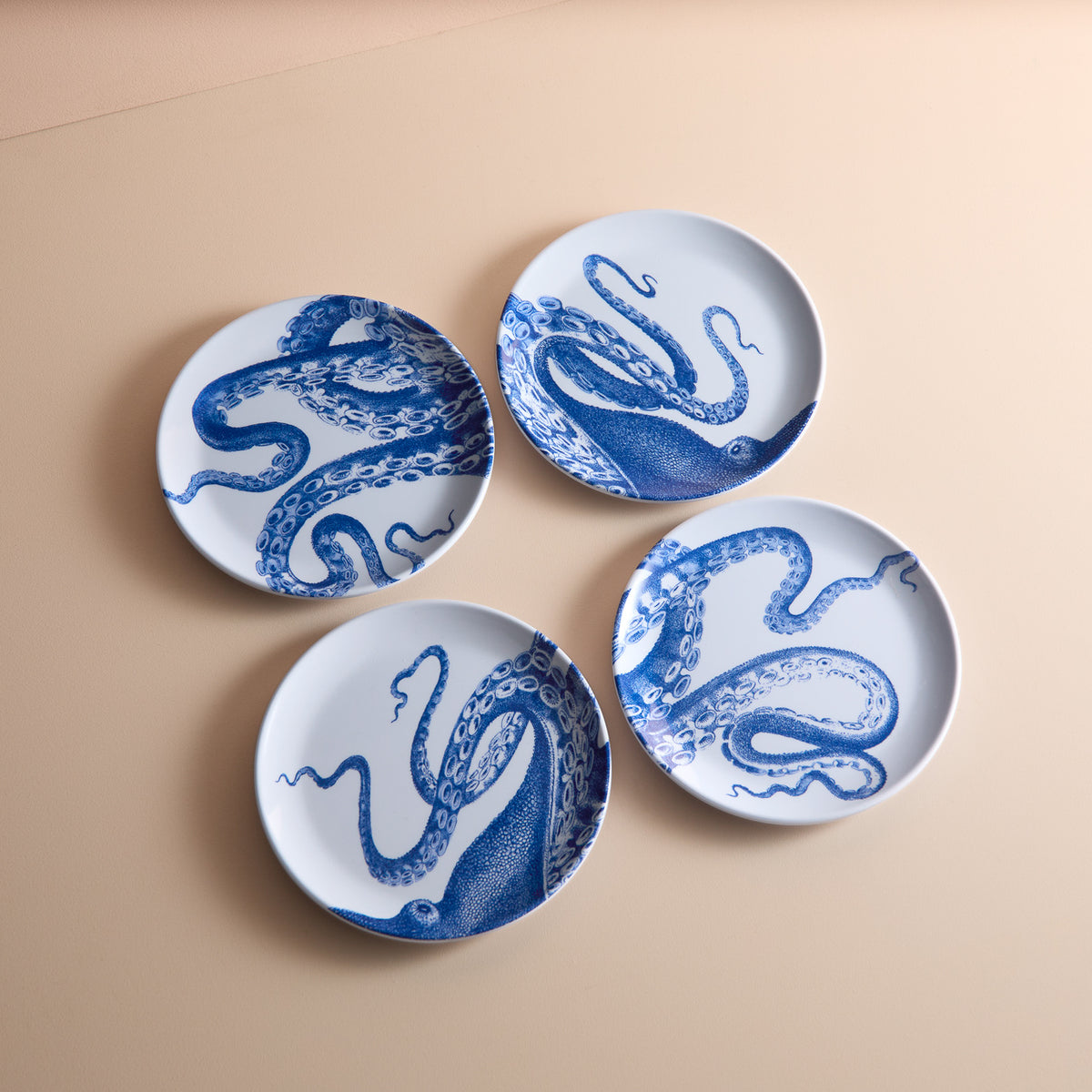 Four Lucy Melamine Small Plates by Caskata, featuring intricate blue octopus designs on white melamine, are elegantly arranged on a beige surface. These BPA-free plates ensure style and safety for your dining experience.