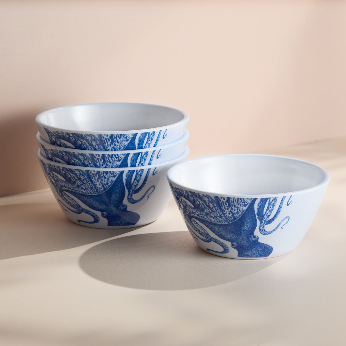 A set of four Caskata Lucy Melamine Cereal Bowls, white with blue octopus designs, is stacked against a beige background.