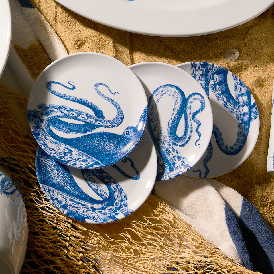 Four Lucy Melamine Small Plates by Caskata, featuring intricate blue octopus designs on white melamine, are elegantly arranged on a beige surface. These BPA-free plates ensure style and safety for your dining experience.