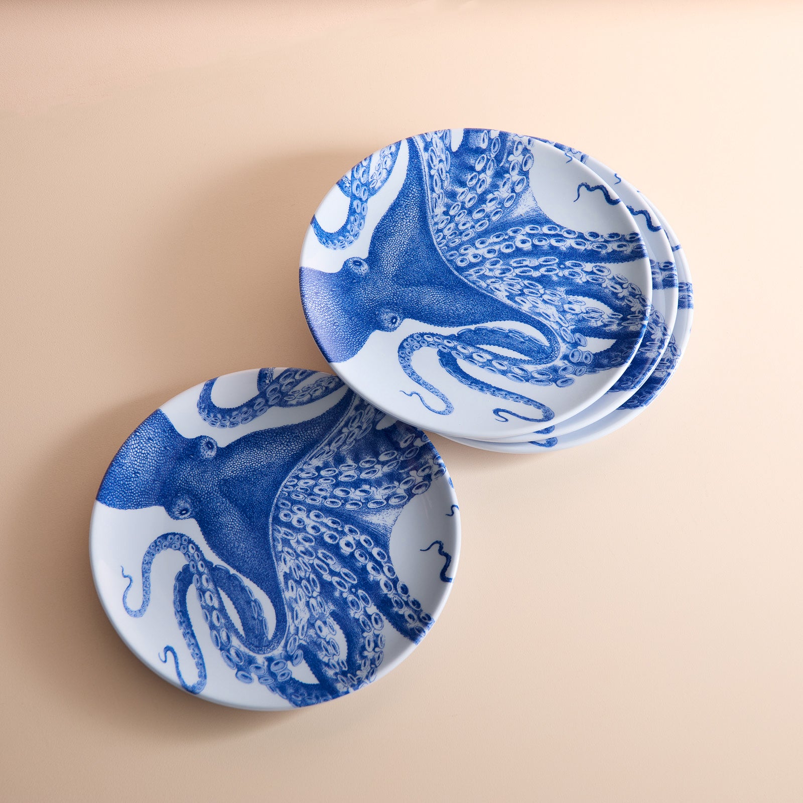 Three plates from the Caskata Lucy Melamine Salad Plates set, featuring BPA-free construction and blue octopus designs, are elegantly arranged on a beige surface.