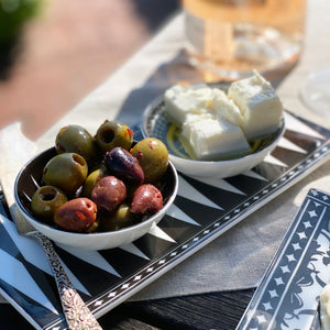 The Marrakech Serving Bundle by Caskata features assorted olives and white cheese cubes on a bone china tray, elegantly paired with stylish dipping dishes and a drink glass, making the perfect appetizer presentation for any gathering.