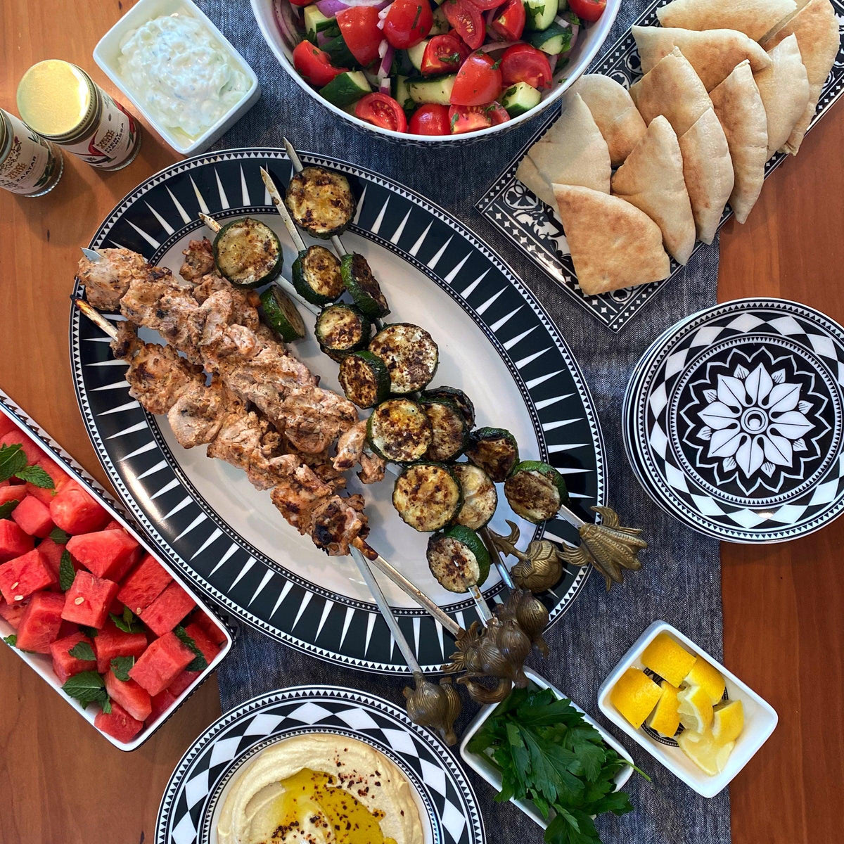 Using the Caskata Casablanca Nested Appetizer Tray &amp; Spoon Set, a delightful spread of grilled skewers, salad, pita bread, watermelon, hummus, lemon wedges, and dipping sauces is elegantly arranged.