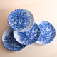 The Peony Melamine Dinner Plates, Set of 4 by Caskata, feature white plates with blue floral designs on a beige surface. Made of BPA-free melamine, these elegant plates add charm and unbreakable style to your table setting.