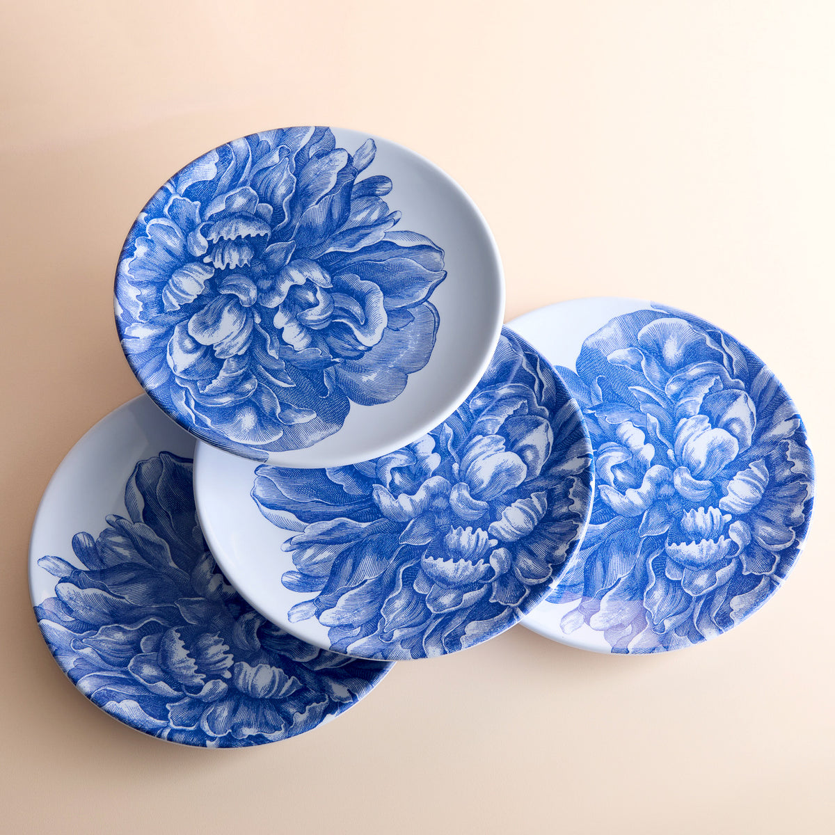 The Peony Melamine Dinner Plates, Set of 4 by Caskata, feature white plates with blue floral designs on a beige surface. Made of BPA-free melamine, these elegant plates add charm and unbreakable style to your table setting.