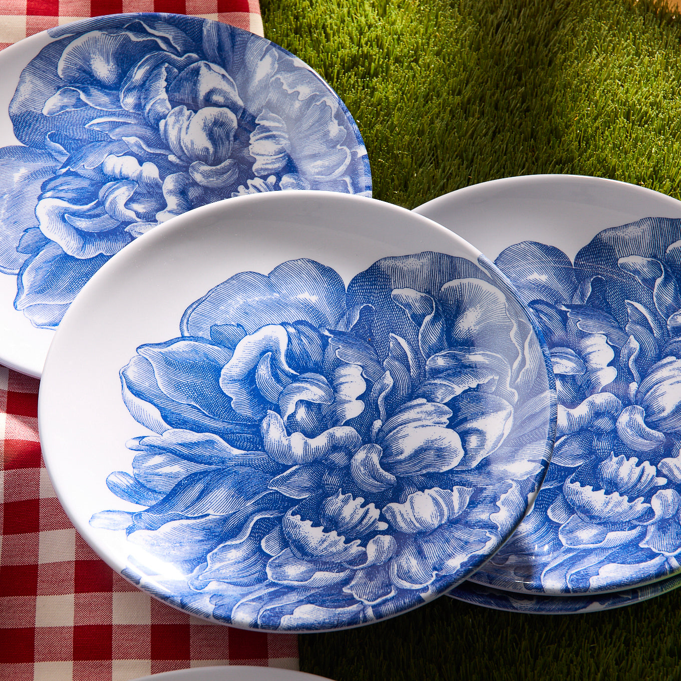 The Peony Melamine Dinner Plates, Set of 4 by Caskata, feature white plates with blue floral designs on a beige surface. Made of BPA-free melamine, these elegant plates add charm and unbreakable style to your table setting.