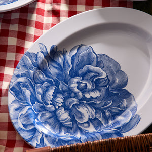 Caskata Peony Melamine Oval Rimmed Platter, featuring an intricate blue peony design, rests on a red and white checkered tablecloth.