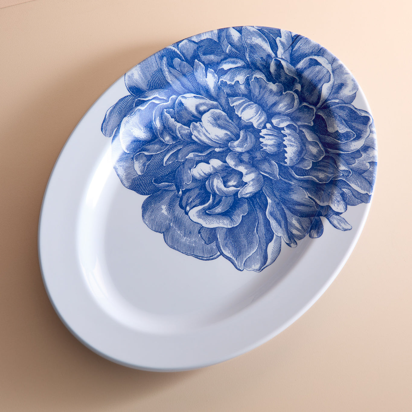 The Caskata Peony Melamine Oval Rimmed Platter features a large blue floral design on a beige backdrop. Made from BPA-free melamine, this elegant and durable piece is perfect for any dining setting.