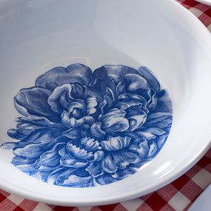 The Caskata Peony Melamine Serving Bowl showcases a blue peony pattern inside, set elegantly atop a red and white checkered surface.