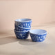 A set of four stacked Peony Melamine Snack Bowls by Caskata, featuring blue and white floral patterns, rests gracefully on a light surface, showcasing the elegance of traditional craftsmanship.