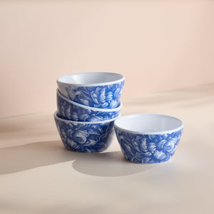 A stack of four Caskata Peony Melamine Snack Bowls, featuring a blue and white delicate peony pattern, sits on a light surface, perfect for adding elegance to your dinnerware collection.