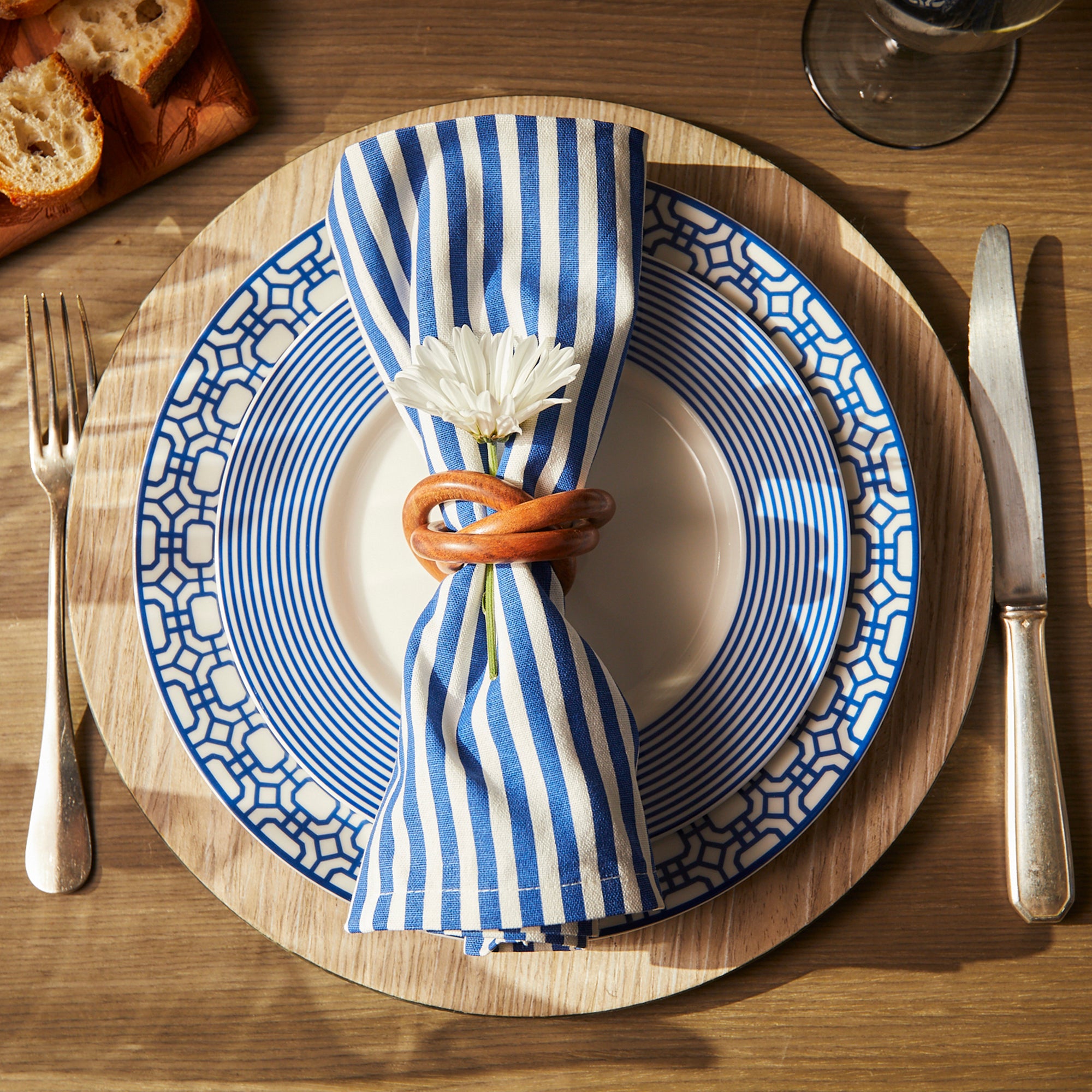 A Newport Garden Gate Rimmed Dinner Plate by Caskata Artisanal Home featuring a geometric blue pattern along the rim, perfect for any contemporary dinnerware or coastal collections.