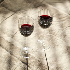 Two Quinn Clear White Wine Glasses by Caskata Artisanal Home sit on a textured surface, sunlight casting shadows on the mouth-blown, lead-free crystal.