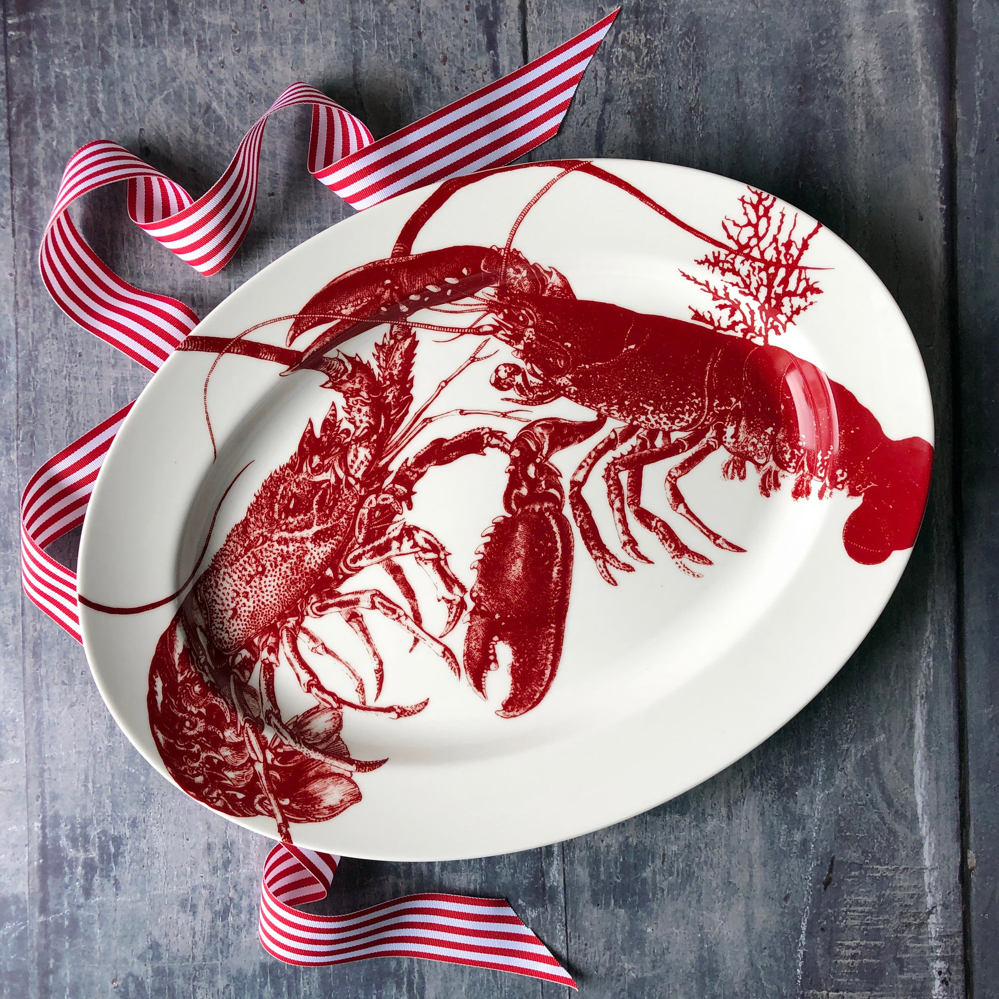 A set of tableware featuring charming red lobster designs, including four lobster mugs, a large lobster platter, and two cloth napkins is now available as the Father's Day Bundle from Caskata.