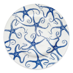 A limited-edition white Starfish Rimmed Dinner Plate from Caskata Artisanal Home features a decorative pattern of blue octopuses intertwined with their tentacles, creating a captivating design.