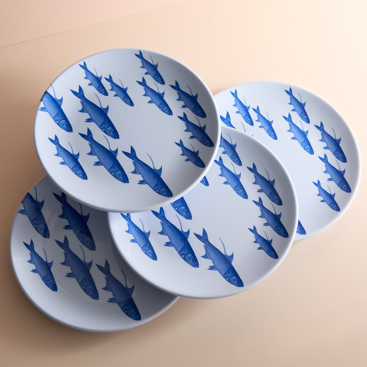 Four BPA-free melamine dinner plates, named &quot;School of Fish&quot; by Caskata, feature a blue fish pattern and are artfully arranged on a light surface, making them perfect for your outdoor collection.