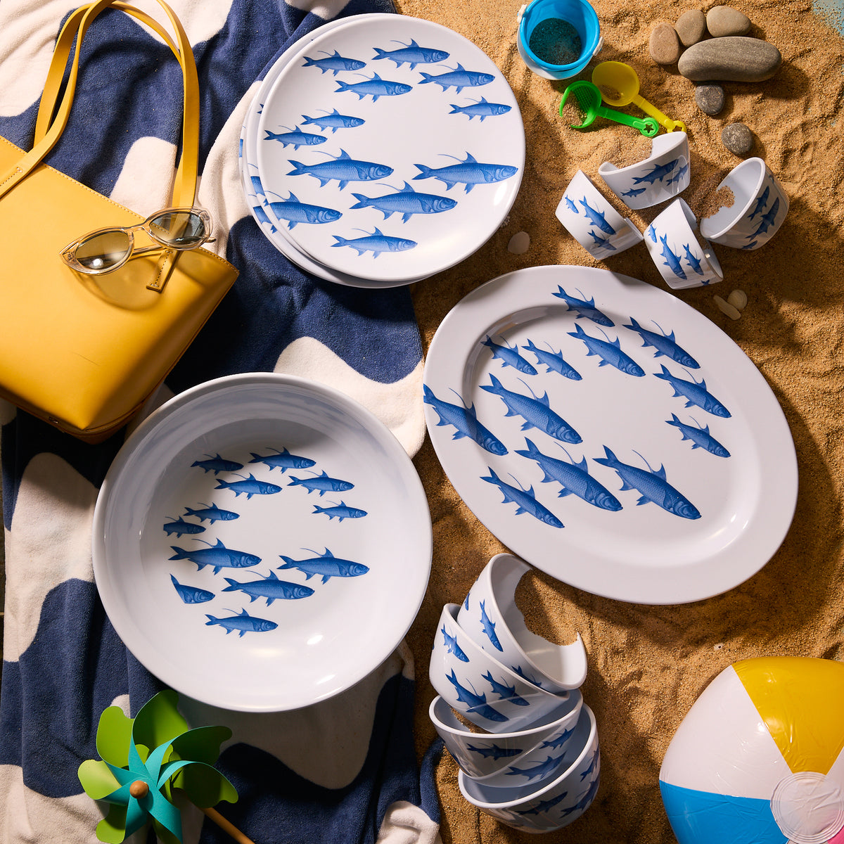 Enhance your coastal setup with Caskata&#39;s School of Fish Melamine Oval Rimmed Platter, BPA-free and sand-patterned. Complete the seaside vibe with a yellow bag, sunglasses, a beach ball, and a pinwheel for added fun.