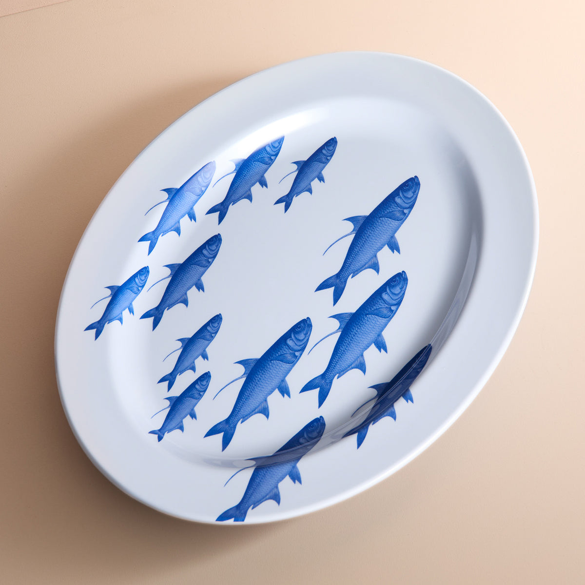 The School of Fish Melamine Oval Rimmed Platter by Caskata is crafted from BPA-free melamine, featuring blue fish swimming diagonally on a beige background. Ideal for adding an artistic touch to your outdoor dinnerware collection.