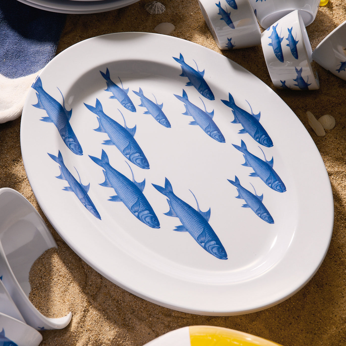 The School of Fish Melamine Oval Rimmed Platter by Caskata is crafted from BPA-free melamine, featuring blue fish swimming diagonally on a beige background. Ideal for adding an artistic touch to your outdoor dinnerware collection.