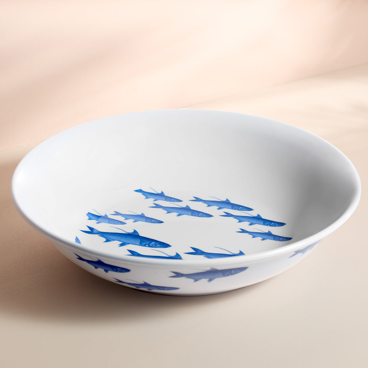 The Caskata School of Fish Melamine Serving Bowl showcases blue fish swimming elegantly in unison on a white surface, perfect for adding whimsy to outdoor gatherings.