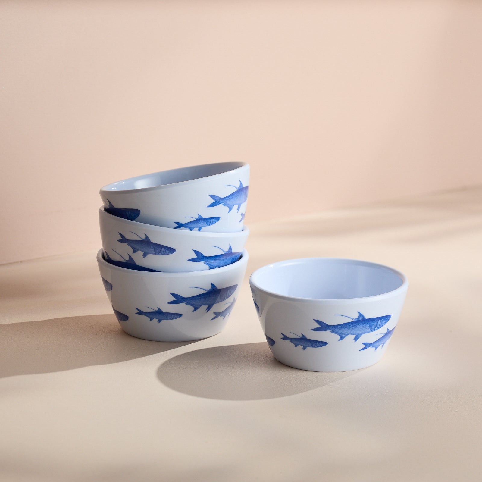 Four Caskata "School of Fish" melamine snack bowls, featuring blue fish illustrations, are stacked beside a single bowl on a light surface.