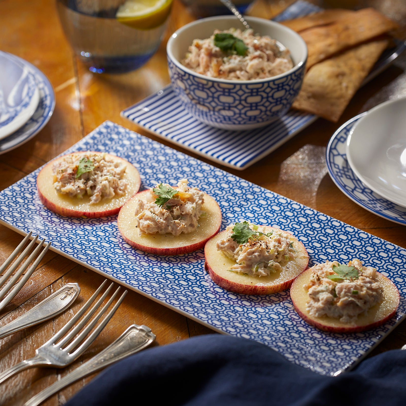 The Newport Serving Bundle by Caskata includes three mats: one with a blue and white geometric pattern and two featuring blue and white stripes. Ideal for serving appetizers on bone china trays, these mats add elegance and ensure easy cleanup.