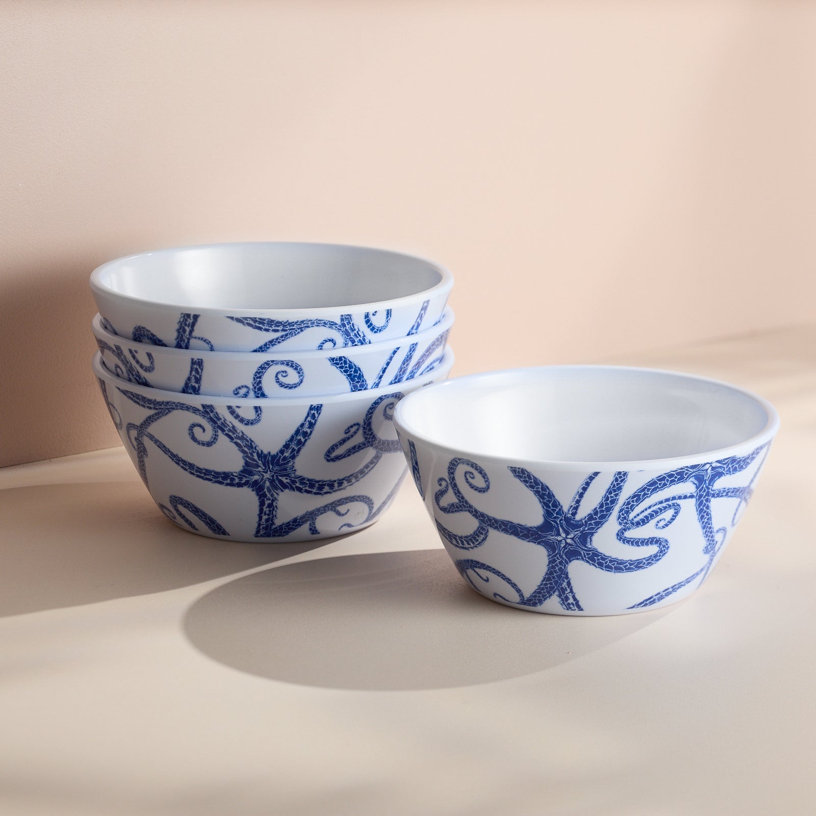 The Caskata Starfish Melamine Cereal Bowls, a set of four, feature charming blue octopus designs on white and are BPA-free. Perfect for outdoor dining, they add seaside charm when stacked on a light surface.