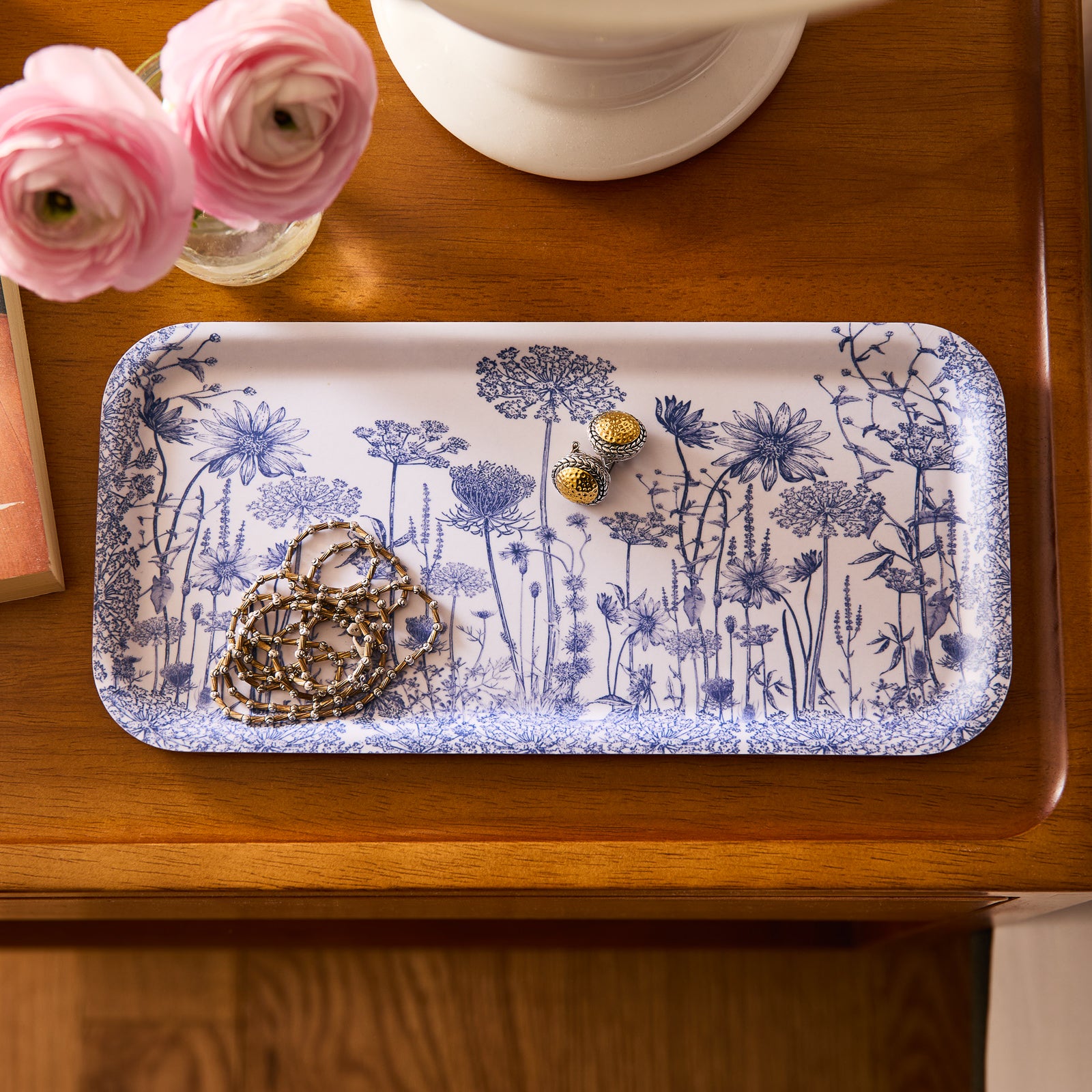 The Caskata Summer Blues Small Rectangular Birchwood Tray showcases detailed blue floral patterns on a white base, adding a summer touch to your gatherings.