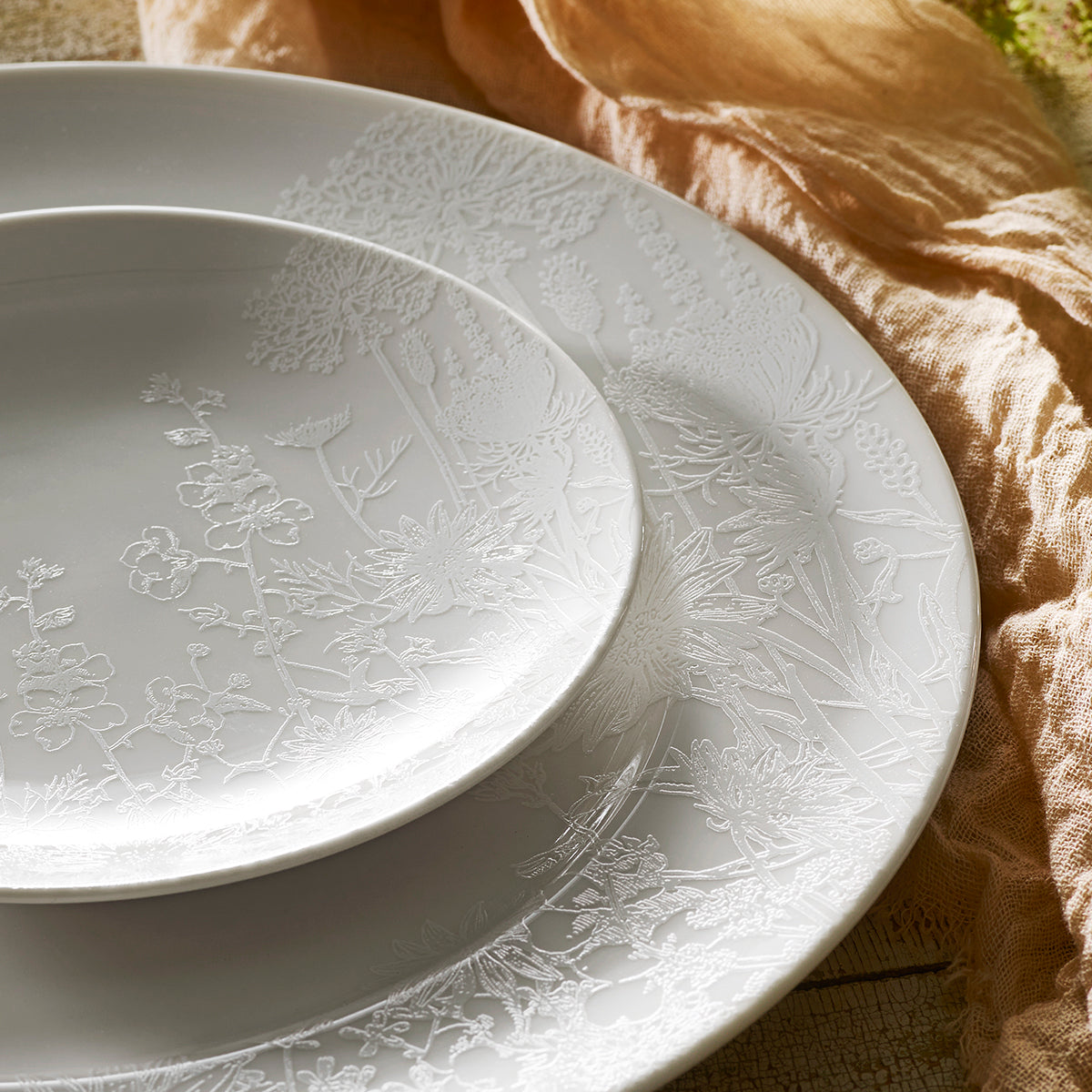 Four Summer Small Plates by Caskata Artisanal Home, crafted from white high-fired porcelain with subtle embossed floral patterns, arranged in an overlapping pattern.